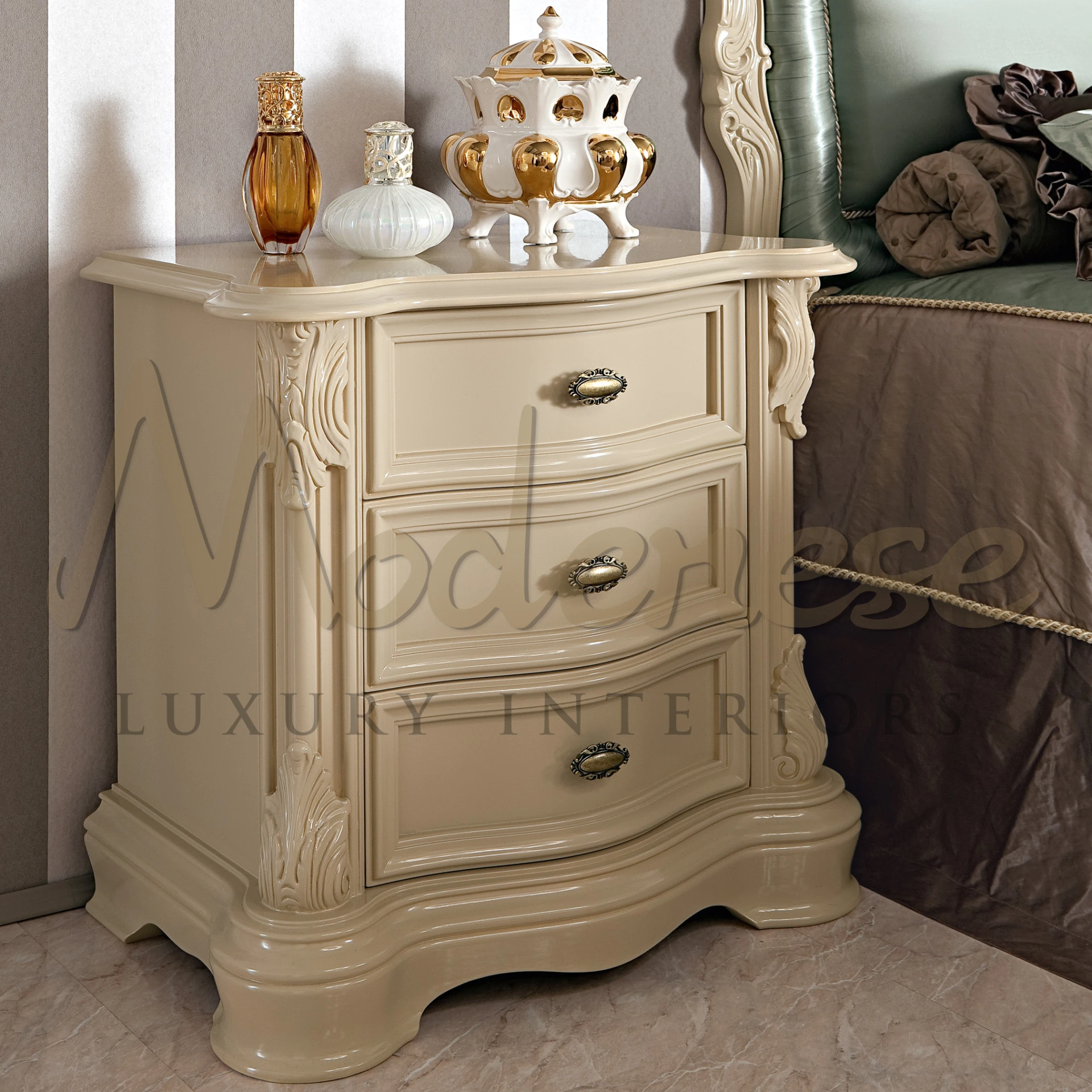 Cream-colored nightstand with detailed carvings and brass hardware, adorned with a decorative items.