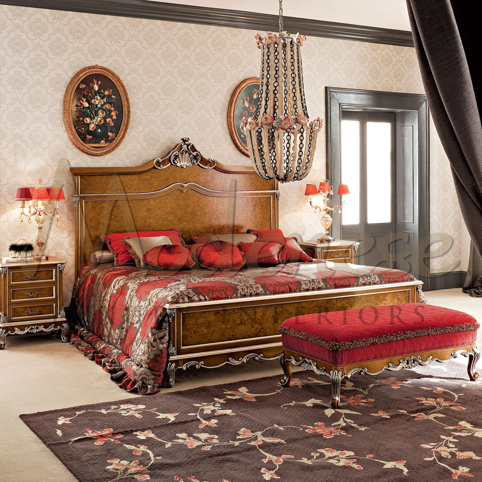 Opulent bedroom featuring a classic bed with burl wood headboard, red and gold bedding, matching drapery, intricate chandelier, floral wall art, and a luxurious red bench at the foot of the bed.