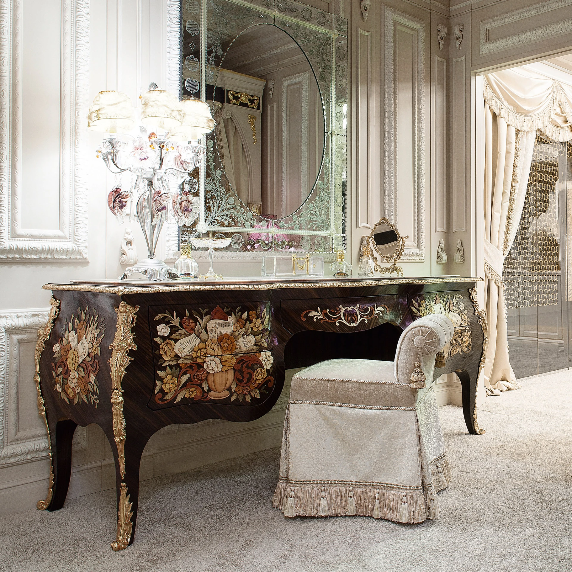 Intricately inlaid wooden dressing table with floral marquetry, gold trimmings, and a matching stool, complete with a glass top and decorative table lamp.