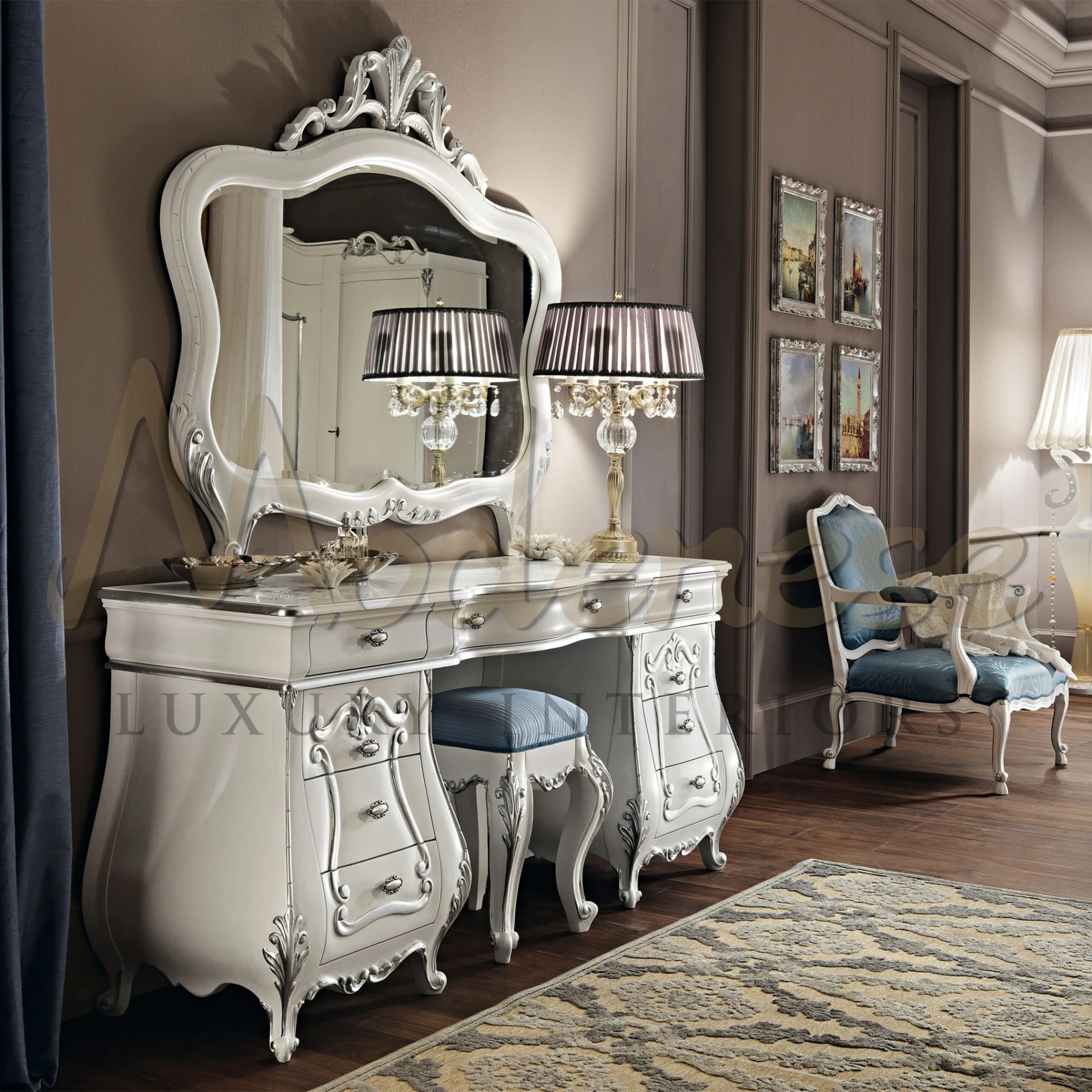 Reflective silver dressing table with ornate carvings and hardware, paired with a stool with blue fabric seat and a classic table lamp with striped shade.