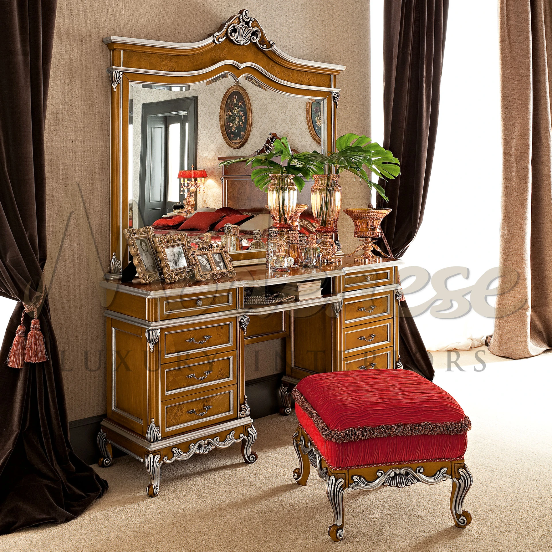 Elegant dressing table in classic wood finish with decorative handles, accompanied by a luxurious red upholstered stool and decorative tabletop items.