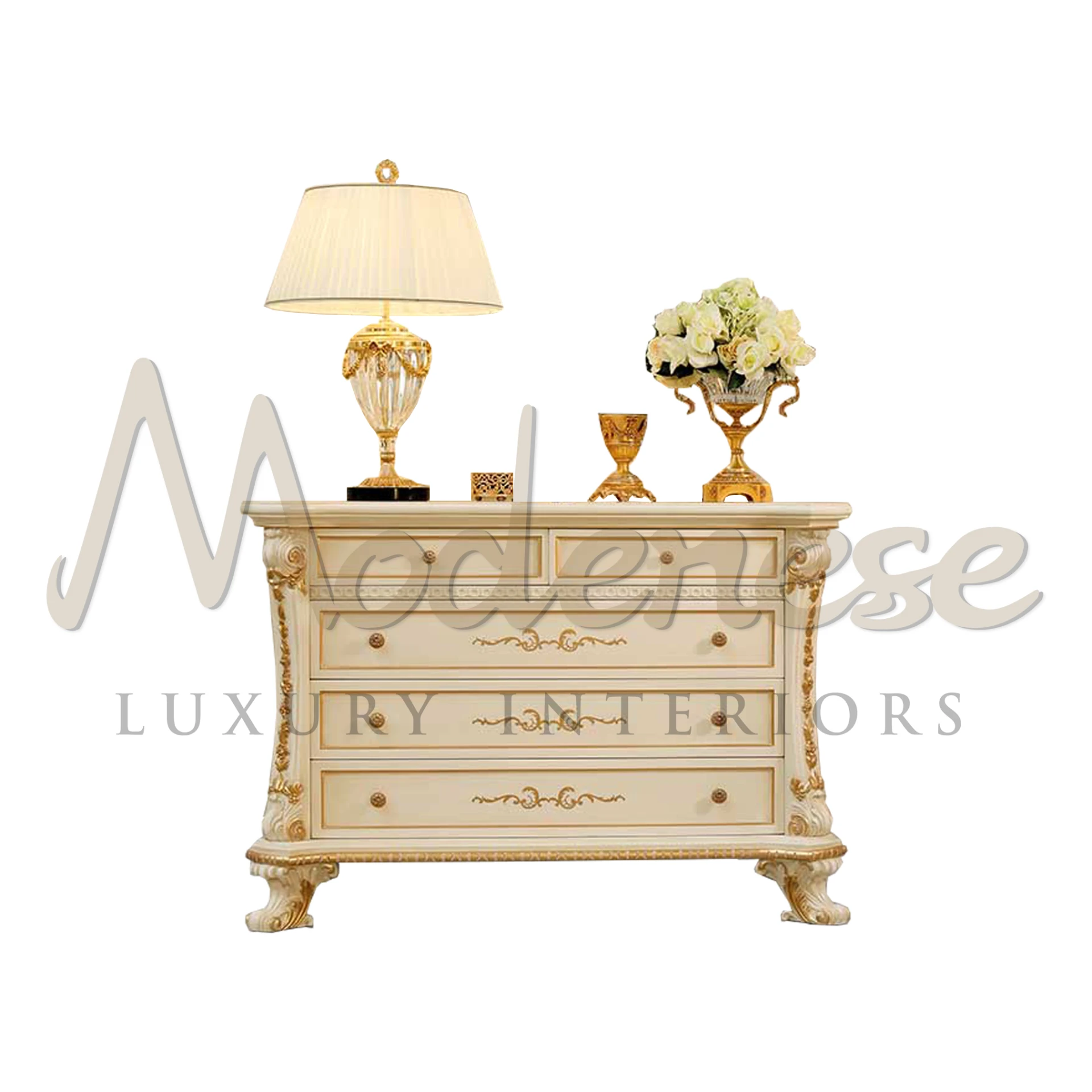 Elegant cream chest of drawers with ornate gold detailing and decorative tabletop accessories including a lamp and a vase of flowers.                     