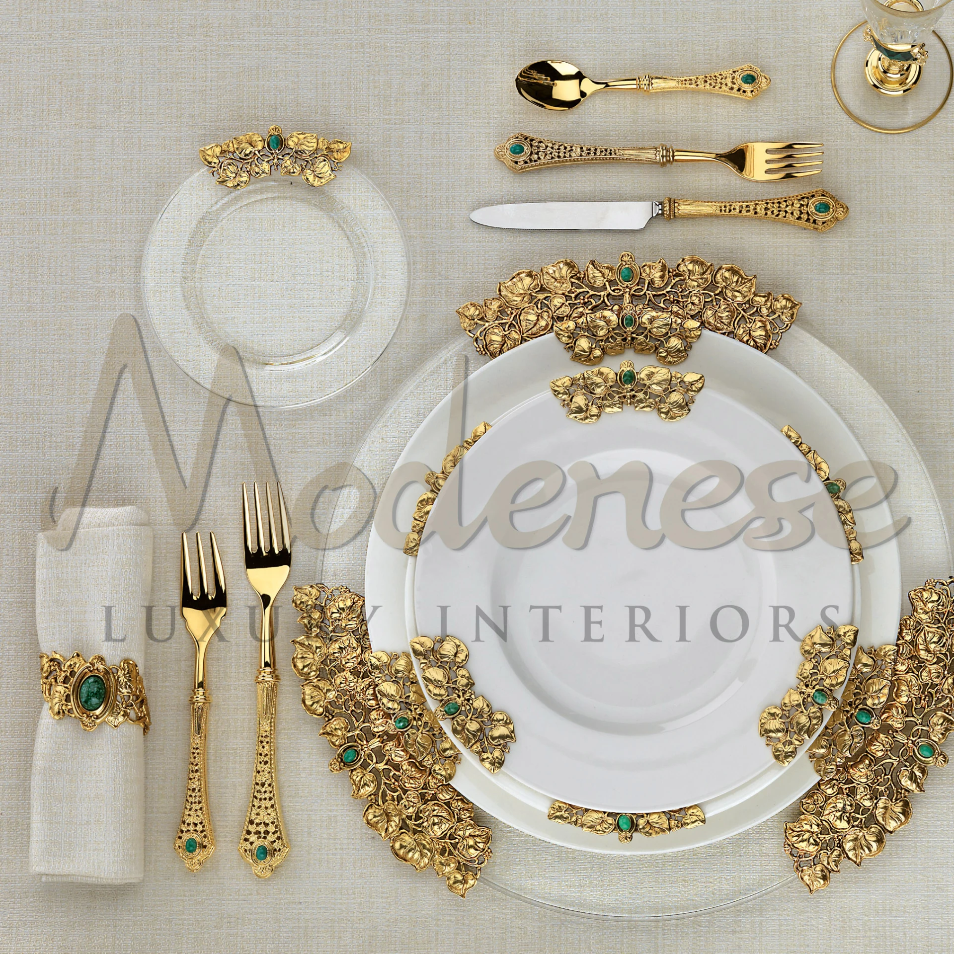 Luxury table setting featuring gold cutlery with intricate designs and emerald accents on a beige tablecloth.