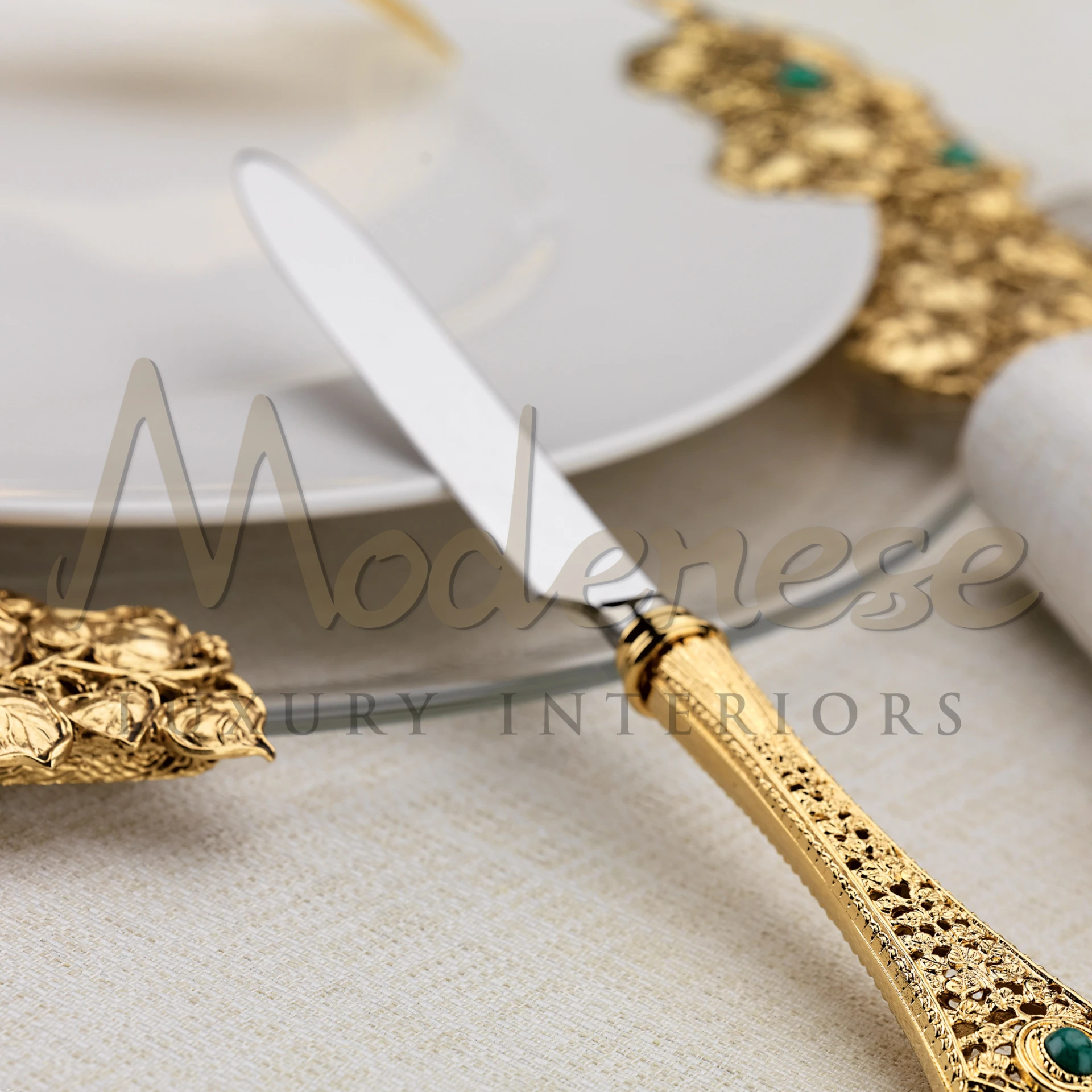 Close-up of a shiny gold knife handle with a pretty green gemstone, part of a fancy table arrangement with fancy plates.