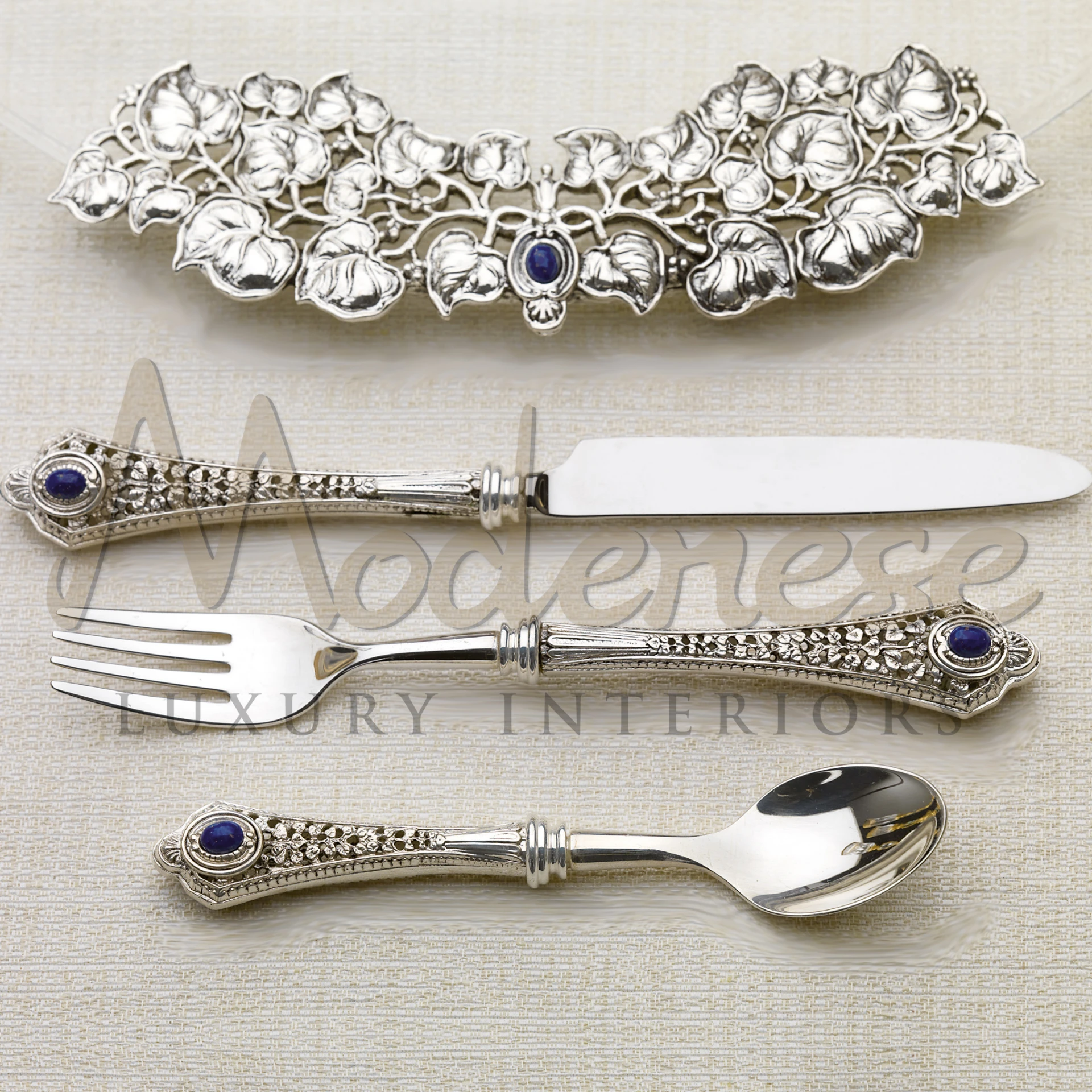 Luxurious silver fork, knife, and spoon with decorative handles and sapphire accents, paired with a floral knife holder