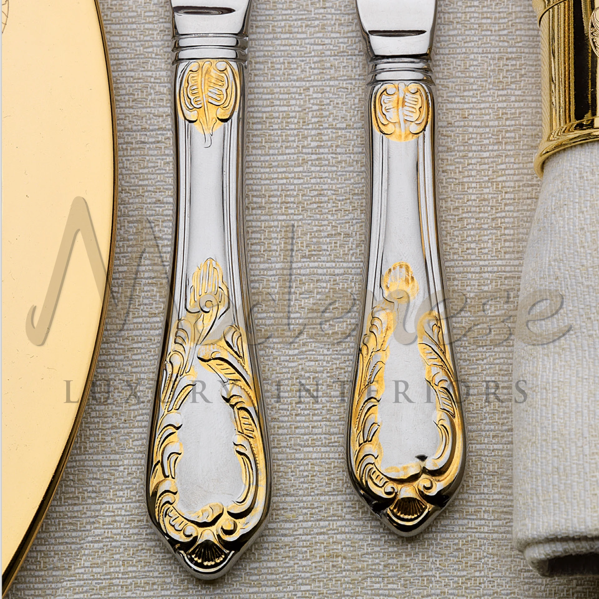 Close-up of silver cutlery handles with gold floral accents on a textured tablecloth