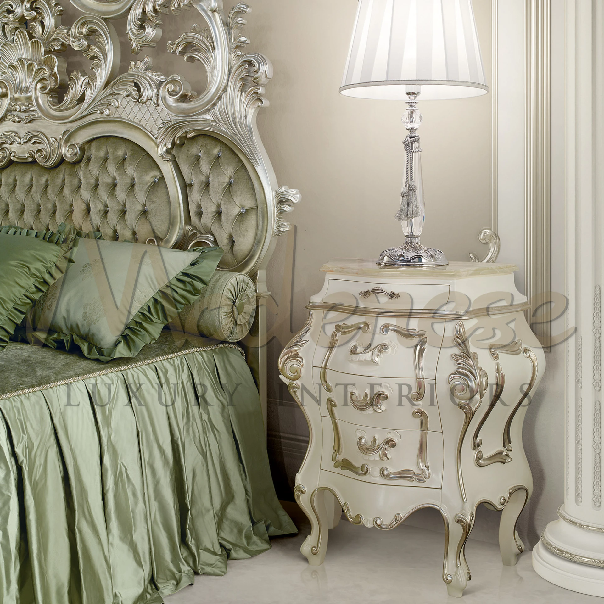 A corner of a sophisticated bedroom featuring a portion of a bed with a tufted olive green headboard boasting elaborate silver carvings. A matching green bedspread contributes to the luxurious feel. 