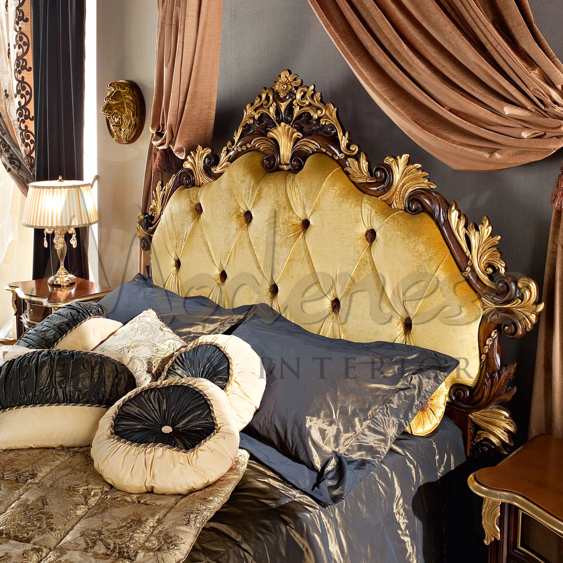 A luxurious bedroom with a golden tufted headboard, detailed dark wooden carvings, draped brown curtains, and elegant bedding with a mix of gold and navy blue pillows.
